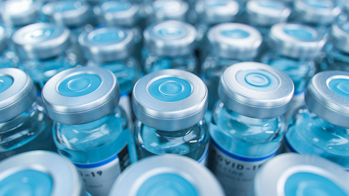 Close-up of multiple vaccine glass vials with silver caps featuring blue centers, clear liquid inside, arranged uniformly.