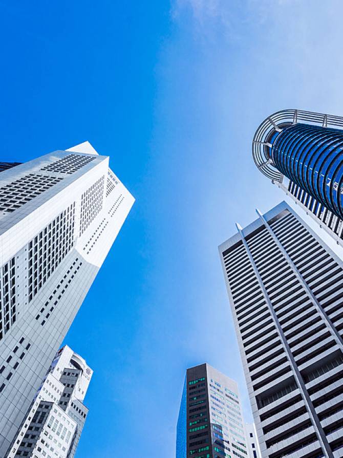 Low-angle view of modern skyscrapers with glass facades and metallic finishes against partly cloudy blue sky, highlighting vertical lines.